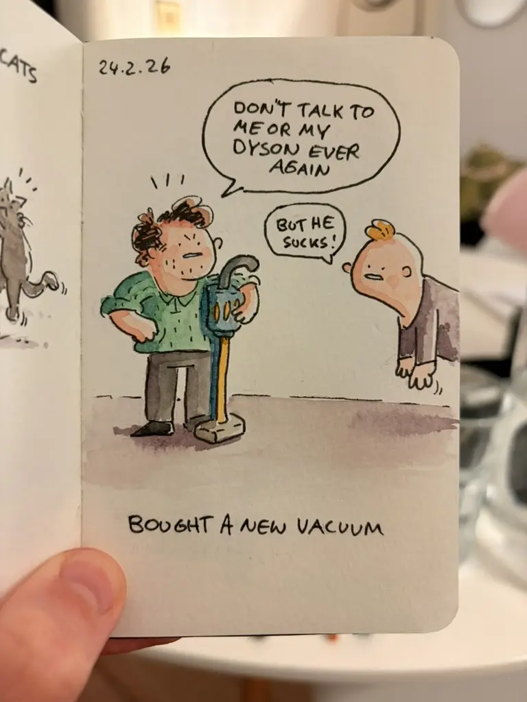 Marcel holds a new vacuum cleaner while a small figure complains about it.